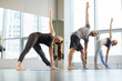 Group of young yoga students standing in row and doing trikonasana while stretching chests at class in modern studio
