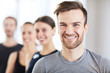 © Seventyfour - Portrait of cheerful handsome young guy with stubble and fashionable hairstyle smiling at camera while standing in line of fitness trainers