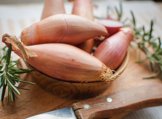 Close-up of shallots in a wooden bowl with fresh rosemary on cutting board