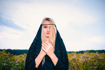 Wall Mural - An attractive blonde girl put on a hood and folded her hands in a praying pose.