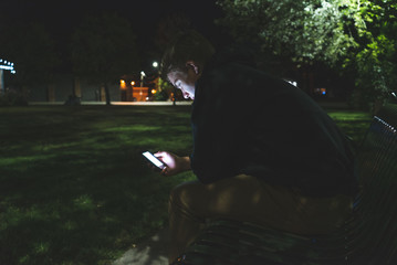 Wall Mural - Depressed teenager on his cellphone while sitting on a park bench at night.