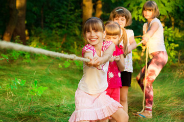 Wall Mural - Group of happy children playing tug of war outside on grass. Kids pulling rope at park.