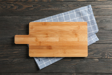 Cutting board with kitchen towel on wooden background, space for text