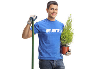 Young male volunteer with a shovel holding a plant