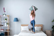 © BestForYou - Young cheerful woman having fun with pillows on the bed at home.