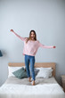 © BestForYou - Young cheerful woman standing on the bed at home.