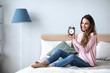 © BestForYou - Happy young woman holding alarm clock on the bed at home.