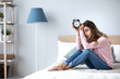 © BestForYou - Sad woman holding alarm clock on the bed.