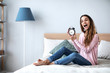 © BestForYou - Happy young woman holding alarm clock on the bed at home.