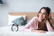 © BestForYou - Beautiful smiling woman with alarm clock on the bed at home.