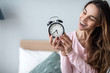 © BestForYou - Joyful woman with alarm clock at home.