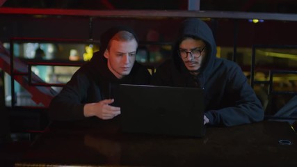 Wall Mural - zoom in of two young multiethnic men in hoodie sitting at laptop in bar and developing software toge