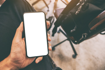 Mockup image of a man's hand holding black mobile phone with blank screen with a cup of coffee on the table in cafe