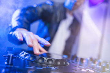 Dj mixing at party festival with blue light and smoke in background - Summer nightlife view of disco club inside. Focus on hand