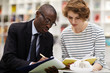 © Seventyfour - Content confident African-American college consultant in formal suit drawing in clipboard while explaining information to student girl in library