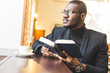 © xartproduction - Young handsome dark-skinned businessman in a cafe reads a book with a cup of tea.