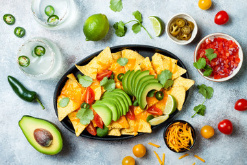 Yellow corn nachos chips with melted cheese sauce, avocado, jalapeno, cilantro leaves, tomato salsa and spicy iced margarita cocktail