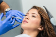 canvas print picture - Attractive young woman is getting a rejuvenating facial injections. She is sitting calmly at clinic. The expert beautician is filling female wrinkles by hyaluronic acid.
