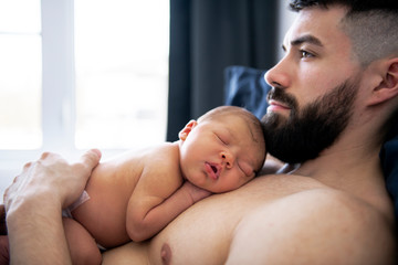 father lay on bed with his newborn baby son lying in