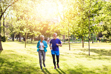 Wall Mural - Happy senior couple jogging outdoors in park.