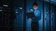© Gorodenkoff - In Dark Data Center: Male IT Specialist Walks along the Row of Operational Server Racks, Uses Laptop for Maintenance. Concept for Cloud Computing, Artificial Intelligence, Supercomputer, Cybersecurity