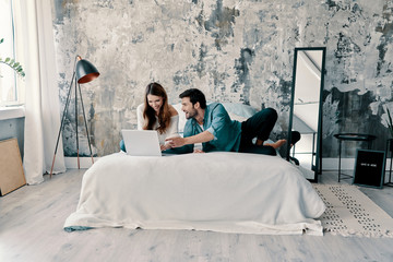 Wall Mural - Looking for a movie to watch. Beautiful young couple using computer while spending time in bed at home