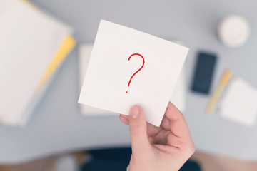 Wall Mural - Woman clerk sitting at the office table and holding note sticker with question mark. Concept.