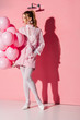 © LIGHTFIELD STUDIOS - beautiful young woman holding air balloons while standing with hand in pocket on pink