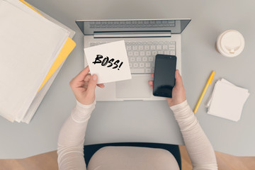 Wall Mural - Woman clerk sitting at the office table and holding note sticker with word boss and the phone. Concept.