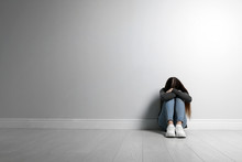 Upset Teenage Girl Sitting On Floor Near Wall. Space For Text