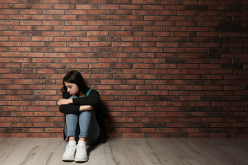 Wall Mural - Upset teenage girl sitting on floor near wall. Space for text