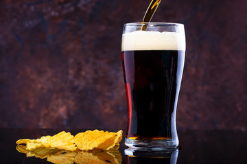 glass of beer with foam and chips on a dark background