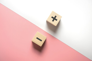 the concept of opposites, wood blog with plus and minus on white and pink background, flat lay, copy