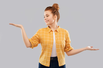 choice and people concept - smiling red haired teenage girl in checkered shirt holding something imaginary on empty hands over grey background