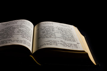 Open hebrew Bible, isolated on black background, with side lighting