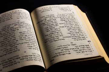 Open hebrew Bible, isolated on black background, with side lighting