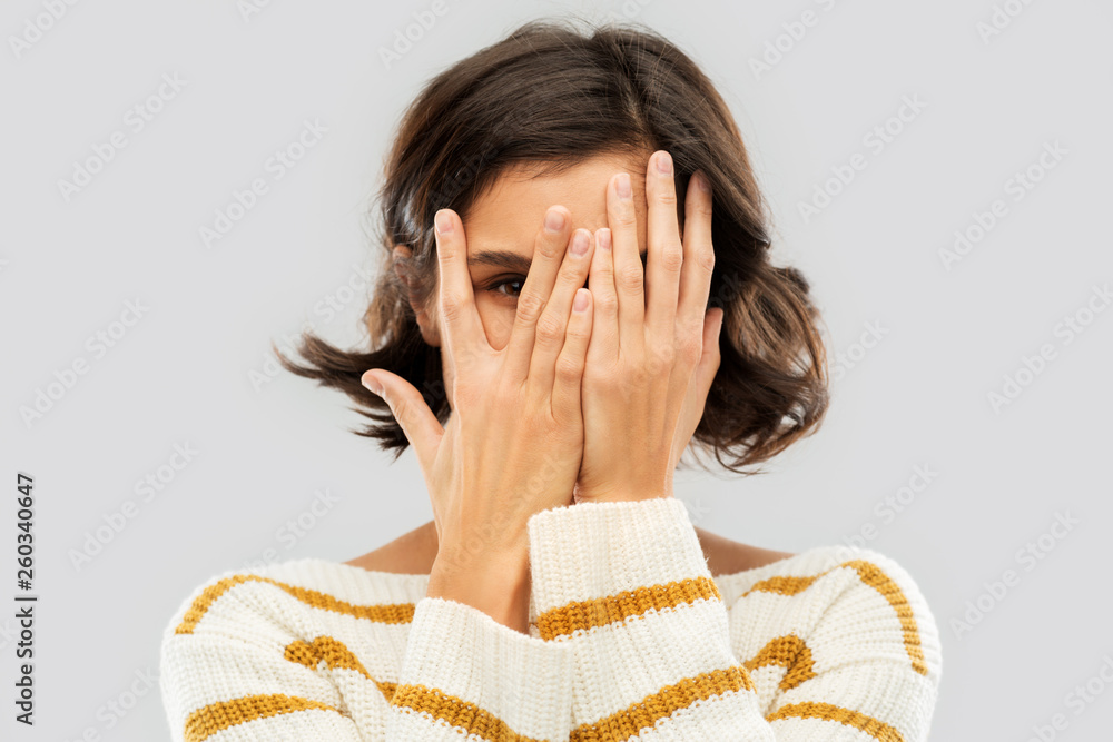 people concept - happy smiling young woman in striped pullover closing face with hands and looking by one eye through her fingers over grey background - obrazy, fototapety, plakaty 