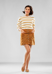 people concept - happy smiling young woman in striped pullover, short skirt and ballet flat shoes posing over grey background