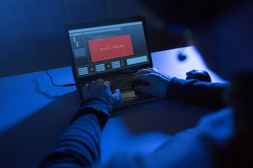 cybercrime, hacking and technology concept - hands of hacker with access denied message on laptop computer making cyber attack in dark room