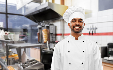 Wall Mural - cooking, profession and people concept - happy male indian chef in toque over kebab shop kitchen background