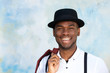 © mimagephotos - Close up handsome young african american man with suspenders and hat smiling by wall