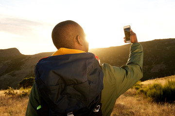 Wall Mural - behind of african american man hiking with cellphone taking selfie in mountains