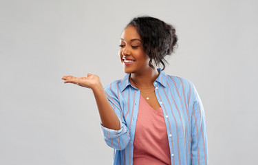 people and advertisement concept - happy african american young woman holding something imaginary on