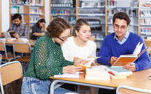 Students Sitting In University Library, Working With Professor