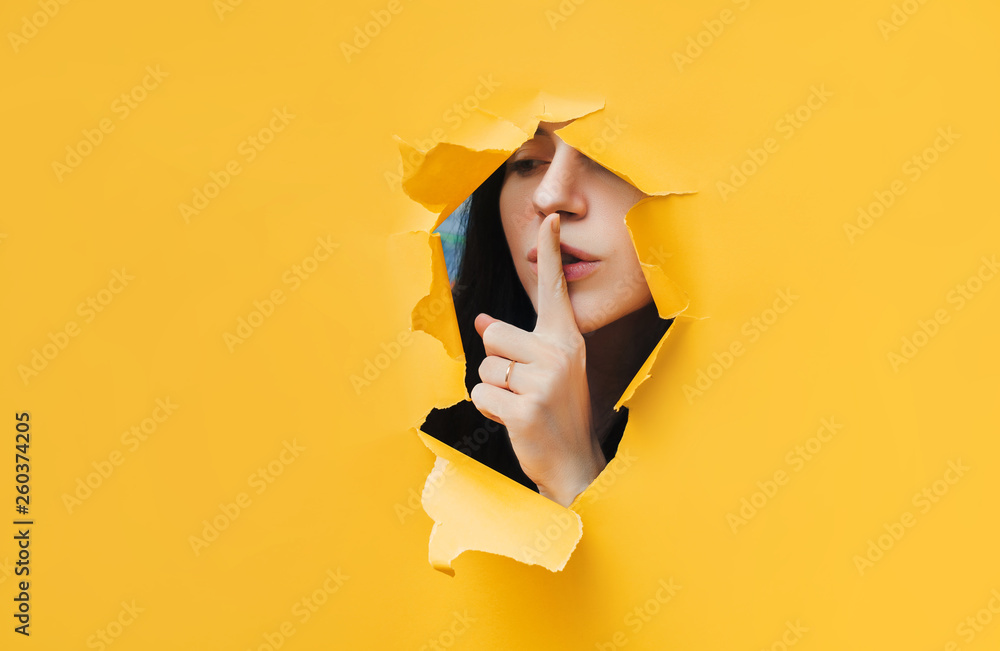 A young girl closes her lips with her index finger,making it clear to the viewer that you need to observe silence,keep a secret and not say too much. Censorship and harassment of freedom of speech. - obrazy, fototapety, plakaty 