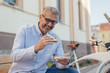 © cherryandbees - middle aged gray haired man sitting bench in the city and eating sandwiches