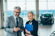 © cherryandbees - salesman showing woman online car gadgets in car dealership showroom