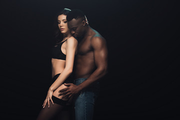 african american man hugging beautiful sexy woman in lingerie isolated on black with copy space