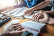 © surachat - Christian group holding hands and praying together around wooden table with open bible page at home, prayer meeting concept.