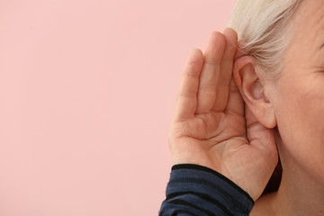 Mature woman with hearing problem on color background, closeup